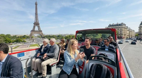 Group of tourists on the upper deck of a red open-top double-decker bus pointing towards the Eiffel Tower in the distance